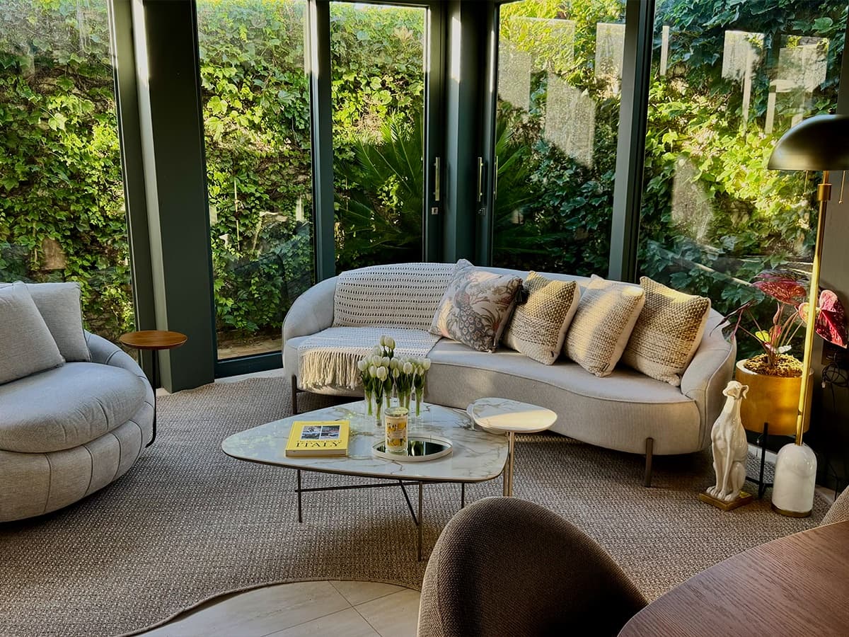 Jardim de inverno com sofá curvo claro, poltrona giratória e mesa de centro em mármore, curadoria UNE Decor